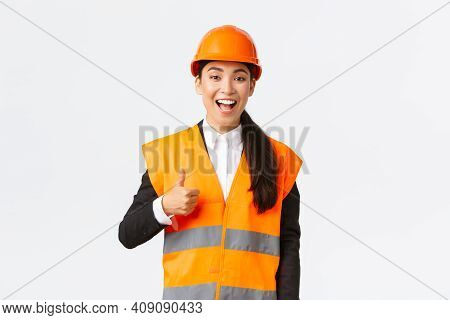 Supportive And Pleased Happy Asian Female Chief Engineer In Safety Helmet Showing Thumbs-up In Appro