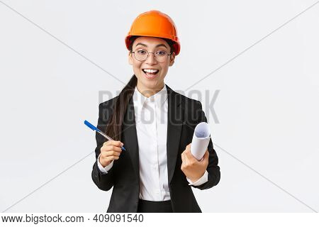 Smiling Professional Female Architect, Asian Engineer In Helmet And Business Suit, Holding Blueprint