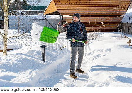 An Adult Man Cleans The Paths In The Garden From Snow In A Good Mood. Shoveling Snow From Paths With