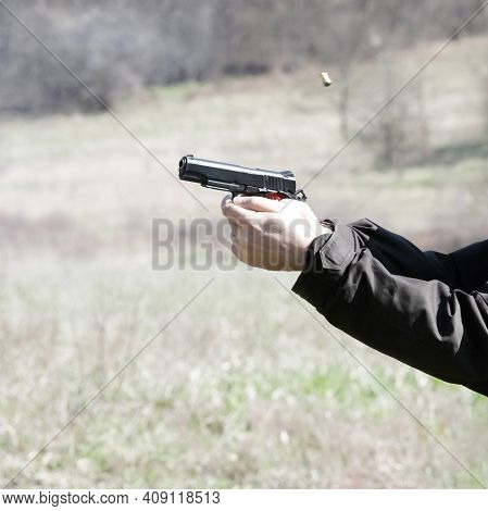 Black Pistol In The Hands Of The Shooter And A Flying Cartridge Case At The Time Of The Shot. A Shor