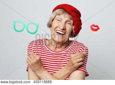 lifestyle, people and party concept: funny grandmother wearing red clothes holding falce glasses and  ready for party