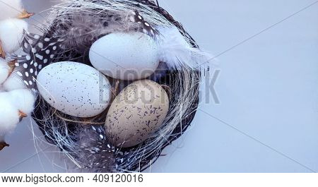 Stylized Happy Easter card,  closeup  with beige and white eggs in nest , polka dot  and white feathers, straw and cotton flowers.