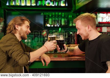 Young man sitting at bar counter and drinking beer together with his friend
