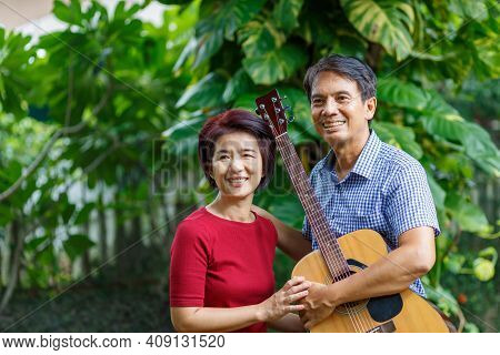 Middle Aged  Couple Playing Guitar While Relax Sitting On Bench In Backyard.
