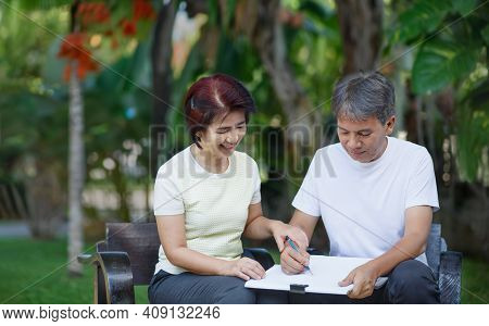 Asian Middle-aged Couple Talking And Designing Garden Plan Together In Backyard.