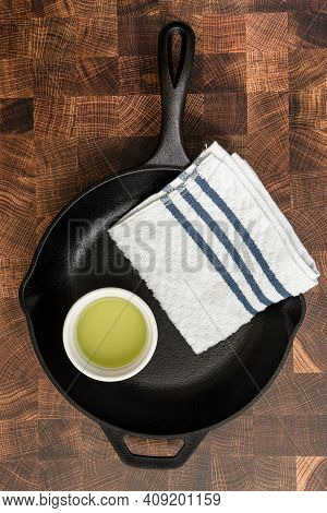 A Cast-iron Skillet Being Prepared To Be Seasoned, With A Cup Of Grapeseed Oil And A Towel On A Cutt