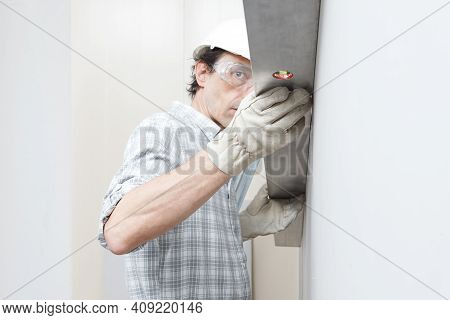 Man Drywall Worker Or Plasterer Checking Level Of White Plasterboard Wall With Bubble Level At Const