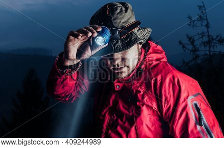 Photo Of A Male Hiker In Red Jacket And Panama Putting On Head Mount Flashlight On Dark Mountain For