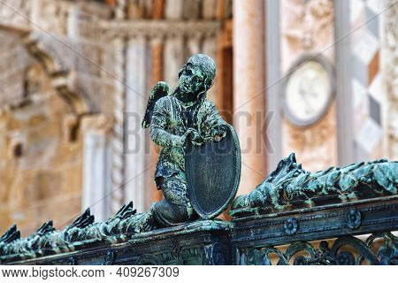 Angel With Armor On The Metal Fence Near The Cappella Colleoni (was Built With Marble Elements Betwe