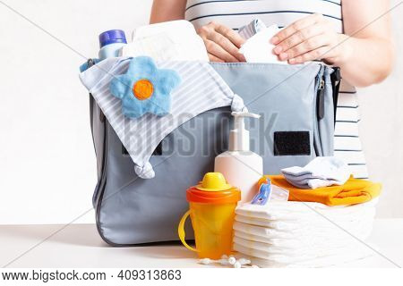 Unrecognizible Pregnant Caucasian Woman In Striped T-shirt Packing Big Blue Diaper Bag To Maternity 