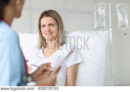 Doctor Examining Woman Lying On Bed In Hospital. Infusion Therapy Concept