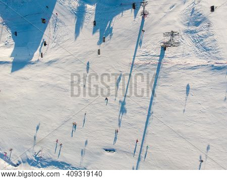 Snowboarders And Skiers Drive Down Ski Slope In Winter Through Fresh Snow, Areal Top View