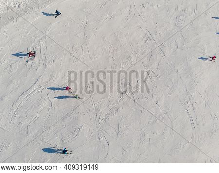 Snowboarders And Skiers Drive Down Ski Slope In Winter Through Fresh Snow, Areal Top View