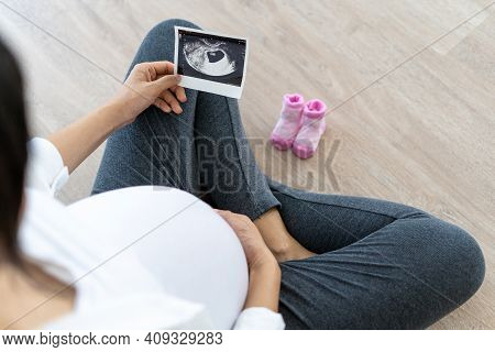 A Pregnant Woman Is Looking At An Ultrasound Photo Of Fetus. Mother Gently Touches The Baby On Stoma
