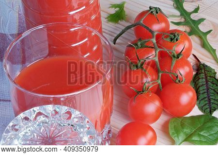 Half Full Glass With Tomato Juice With Pulp Stands On A Table Next To Tomatoes On A Branch Close-up 