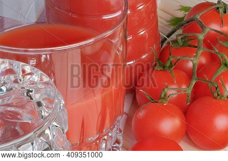 Half Full Glass With Tomato Juice With Pulp Stands On A Table Next To Tomatoes On A Branch Close-up 