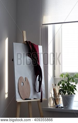 An Easel With A Clean Canvas Board And A Palette Are Ready For New Work. Artist's Workshop. Brushes 