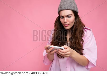 Photo Of Attractive Concentrated Young Brunette Woman Wearing Stylish Pink Shirt And Grey Hat Isolat