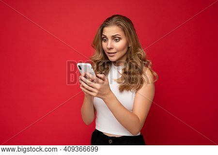 Amazed Shocked Beautiful Young Blonde Woman Wearing White T-shirt Isolated Over Red Background Using