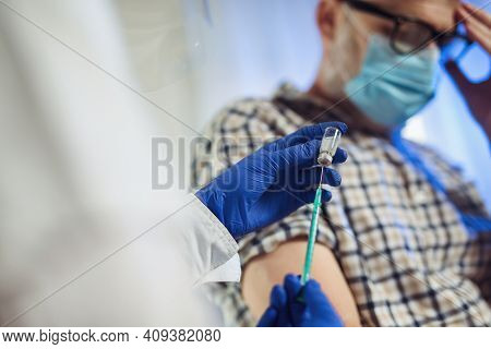 Young Woman Nurse With Surgical Mask And Face Shild Giving Injection To Senior Man. Covid-19 Or Coro