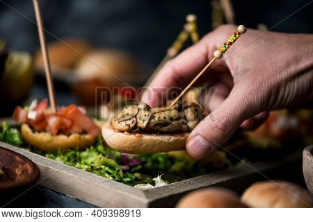 a young caucasian man takes a vegan spanish pincho from a tray with some other pinchos, made with bread with different toppings, served as snacks or appetizers