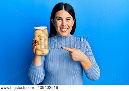 Beautiful brunette woman holding bottle with boiled potatoes smiling happy pointing with hand and finger 