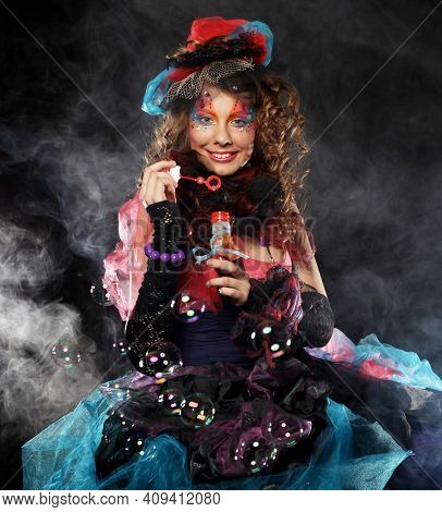 Fashion female model with creative make-up and curly hair blowing soap bubbles. Doll style.