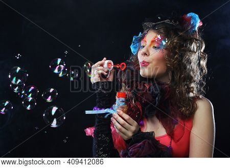 Fashion female model with creative make-up and curly hair blowing soap bubbles. Doll style.