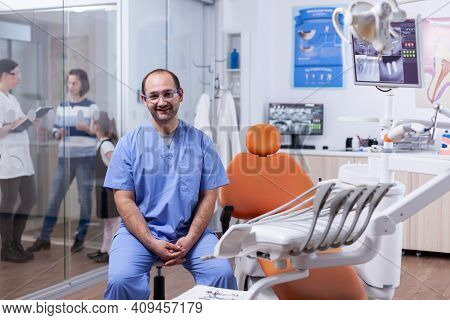Stomatolog In Professioanl Teeth Clinic Smiling Wearing Uniform Looking At Camera. Dentist Doctor Di