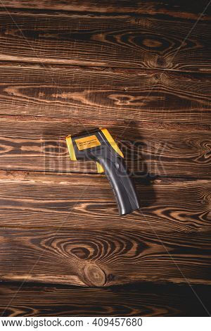 Yellow-black Pyrometer On A Wooden Background. A Device For Non-contact Temperature Measurement. Stu
