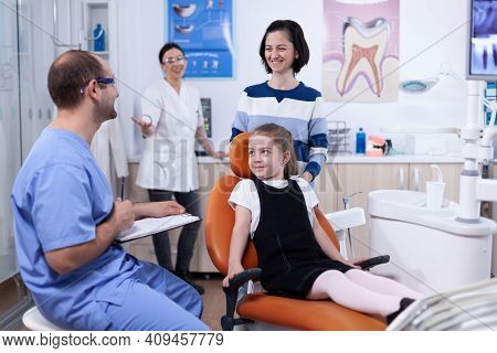 Dentist Assistant Giving Good News To Kid Parent After Teeth Examination In Dental Office. Child Wit