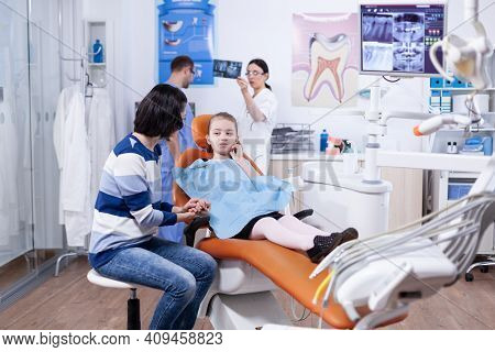 Kid Holding Hand On Face Because Of Pain After Dentist Treatment Looking At Parent. Child With Her M