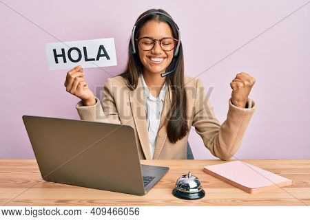 Beautiful hispanic woman wearing operator headset holding hola greenting screaming proud, celebrating victory and success very excited with raised arm 