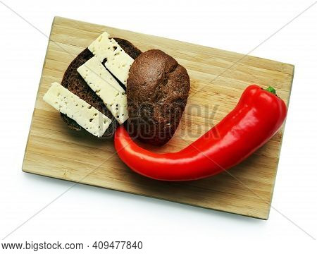 Still Life With Red Ramiro Pepper, Brown Bread And Cheese Slices On The Wooden Cutting Board Against
