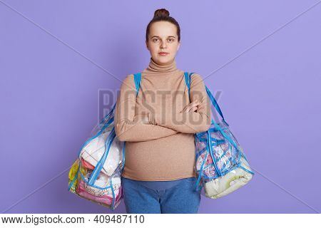 Serious Pregnant Woman With Arms Crossed On Her Chest, Looks At Camera, Dresses Beige Sweater And Je