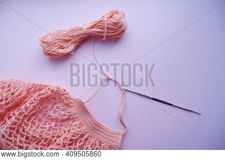 The Process Of Creating A String Bag. A Pink String Bag, A Knitting Hook, And A Skein Of Yarn . Reus