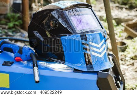 Modern Welding Machine In Blue And Protective Helmet