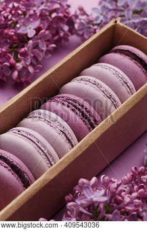 Set Of Violet And Lilac Macarons In Cardboard Gift Box With Lilac Flowers On Violet Background. Clos
