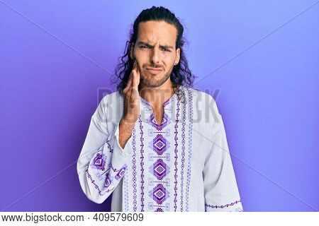 Young handsome man with long hair wearing bohemian and hippie shirt touching mouth with hand with painful expression because of toothache or dental illness on teeth. dentist 
