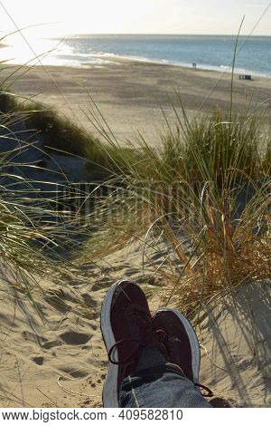 Resting Between The Dunes, Lying On The Beach With Sneakers, With A View Of The Sea On The North Sea