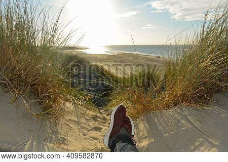 Resting Between The Dunes, Lying On The Beach With Sneakers, With A View Of The Sea On The North Sea