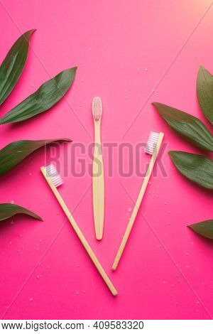 Bamboo Toothbrushes On A Pink Background. Green Leaves. Eco Products. No Plastic. Health And Medicin