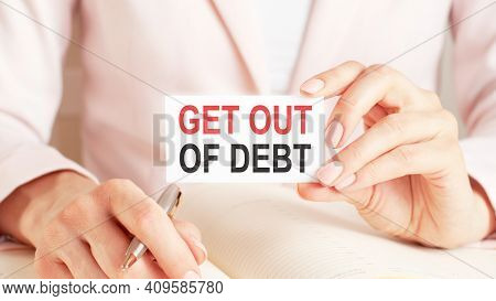 Woman Writes In A Notebook With A Silver Pen And Hand Hold Card With Text: Get Out Of Debt. Pink Bac