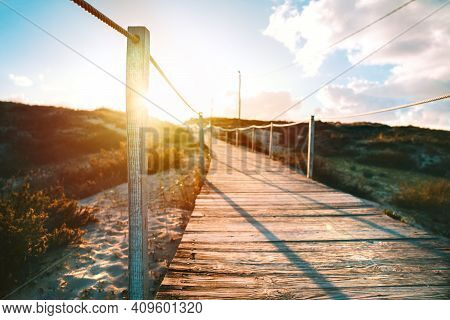 Wooden Pathway To The Sandy Beach And Ocean With Bright Sunbeams At Sunset Or Sunrise. Costa Da Capa