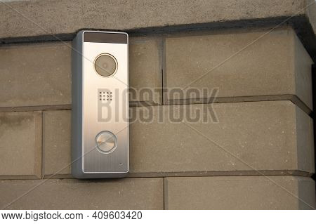 Silver Intercom Panel With Video Camera, On A Brick Beige Fence Pillar Of A Private House