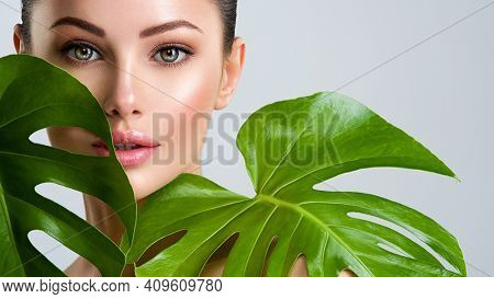 Young beautiful woman with green leave near face and body. Skin care beauty treatments concept.  Closeup girl's face with green leave. White model with clean, health skin of face - posing at studio