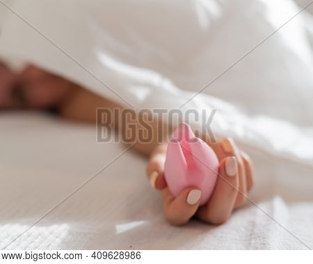 A Faceless Woman Lies In Bed Under A Blanket Holding A Clitoral Vibrator. The Girl Masturbates