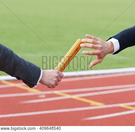 Businessmen Pass On The Baton In Relay Race In Stadium