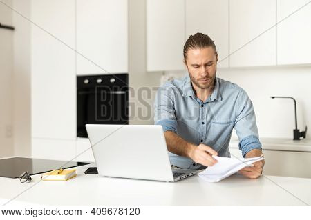 Serious Businessman Frown While Examining Documents, Sitting On The Kitchen At The Laptop, Home Offi