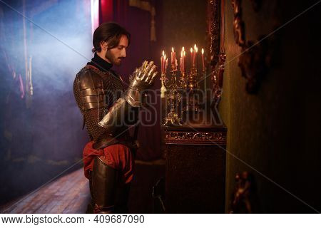 Medieval knight in armor reads a prayer in the castle before the battle. Reconstruction of the atmosphere of the Middle Ages.